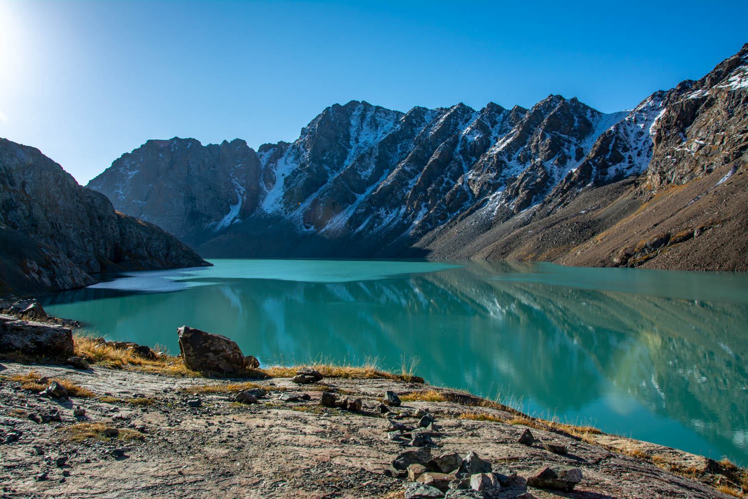 Turquoise glacial waters of Ala-Kul lake surrounded by rocky mountain peaks