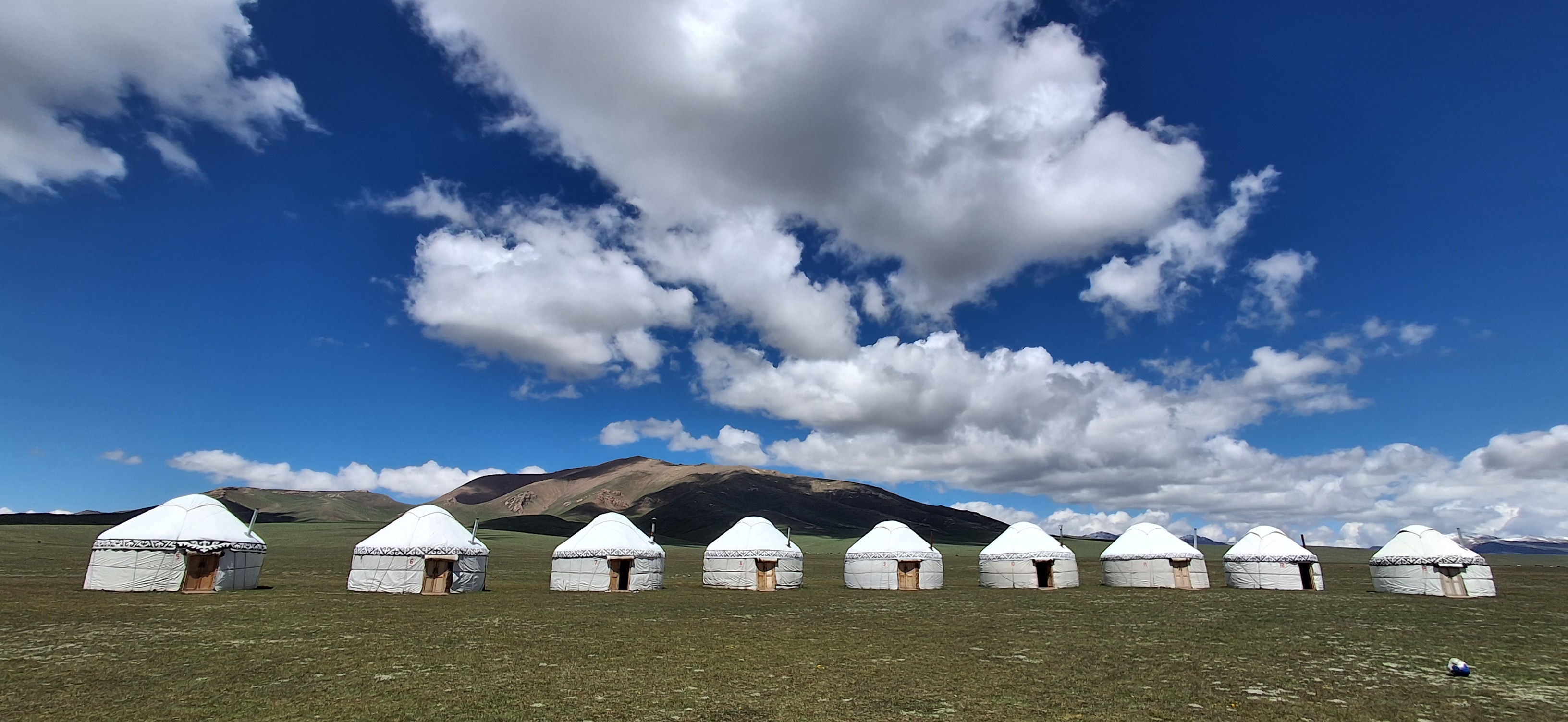 Traditional Kyrgyz yurt camp in a mountain meadow under blue sky